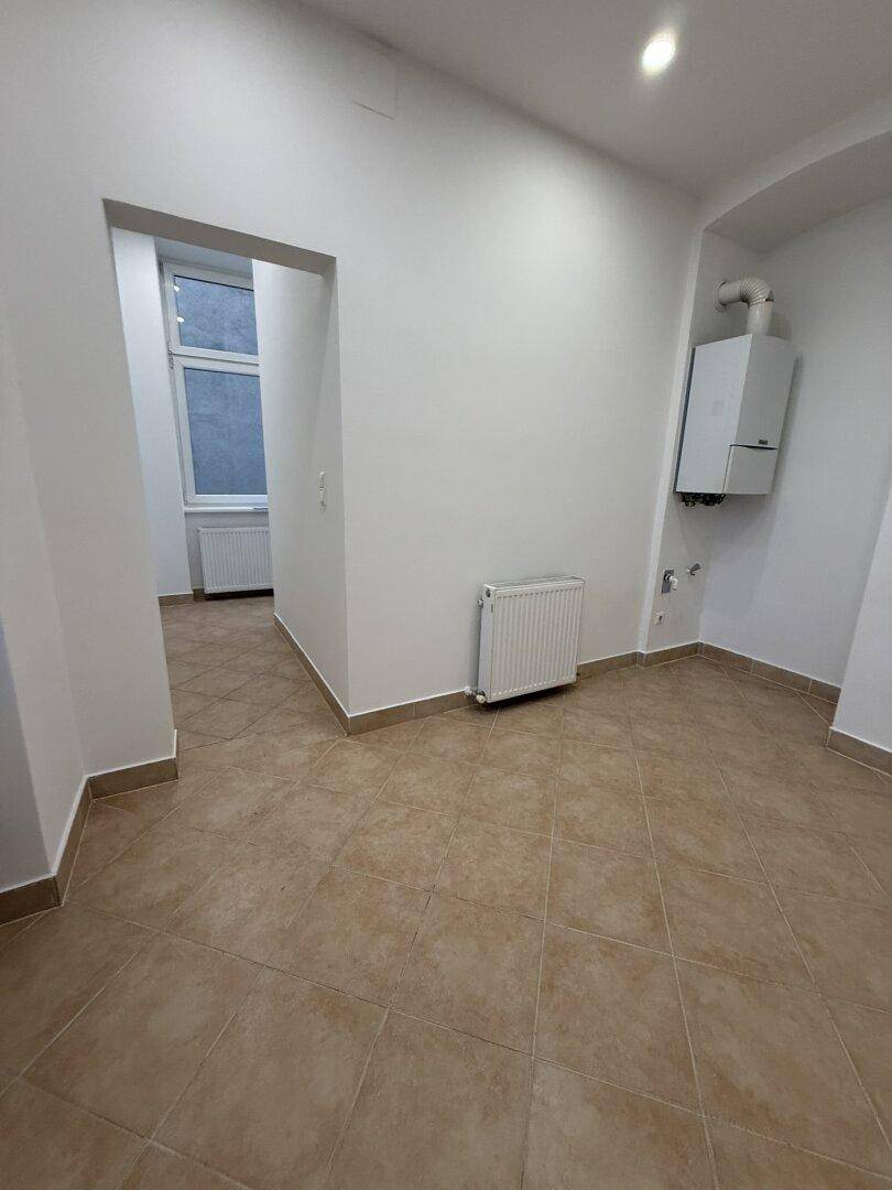 Gefliester Raum mit Heizkörper und Gastherme an der Wand, ideal als Hauswirtschaftsraum.