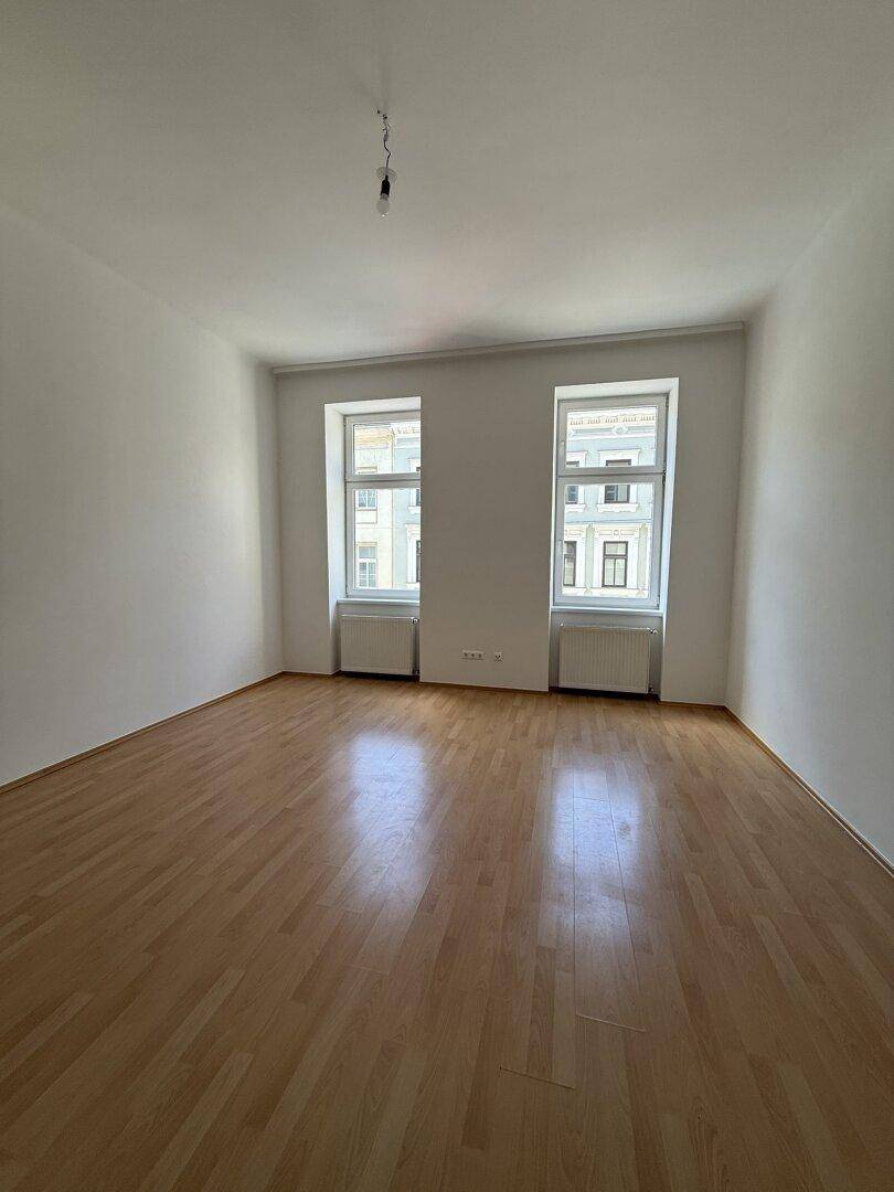 Heller, leerer Raum mit Holzfußboden und zwei großen Fenstern, bereit zur Einrichtung.