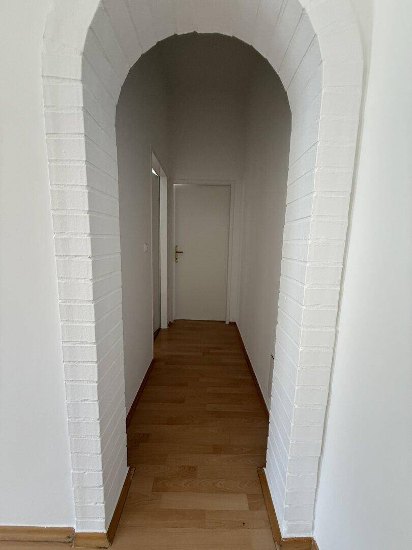 Flur mit Holzfußboden und einem dekorativen gemauerten Rundbogen, der zu weiteren Räumen führt.
