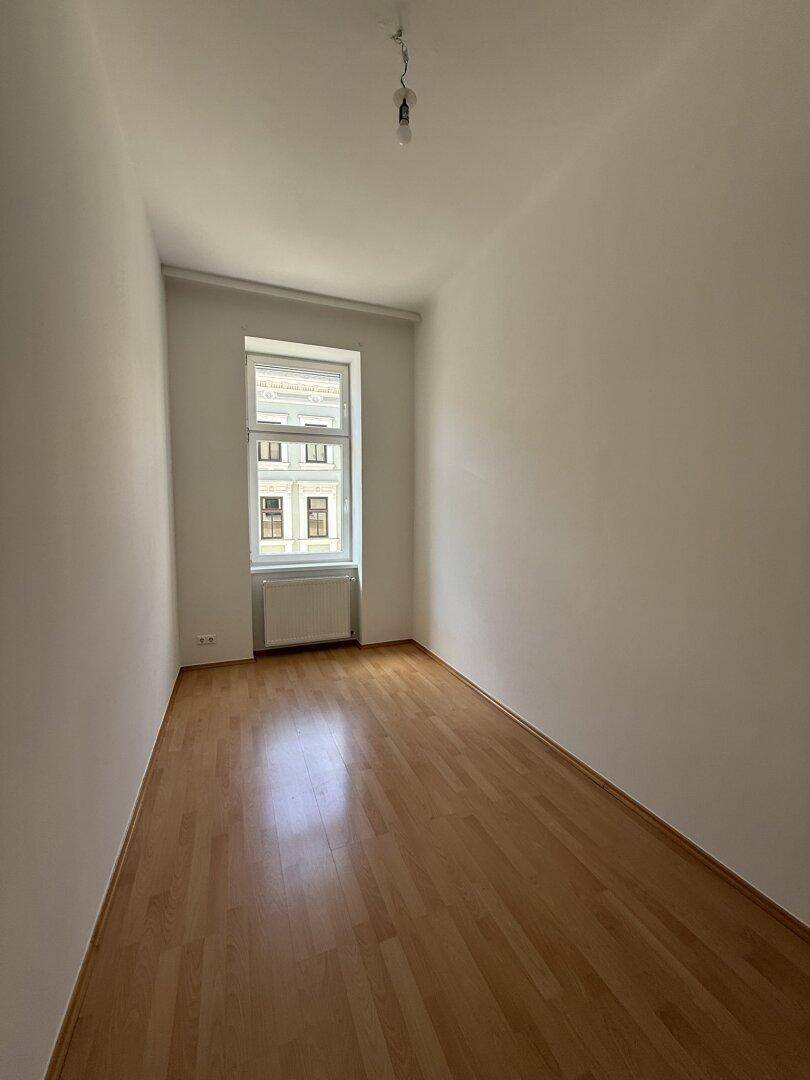 Heller, schmaler Raum mit Holzfußboden und einem Fenster, ideal als Kinder- oder Arbeitszimmer.