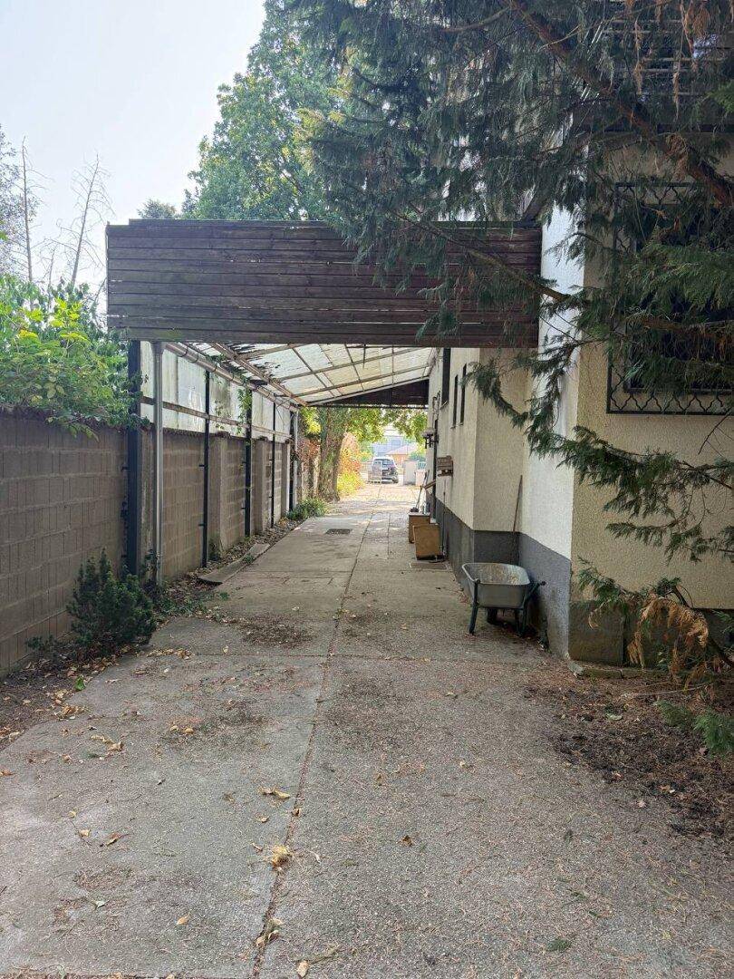 Langer, schmaler gepflasterter Weg, teilweise überdacht, mit Mauern an beiden Seiten.