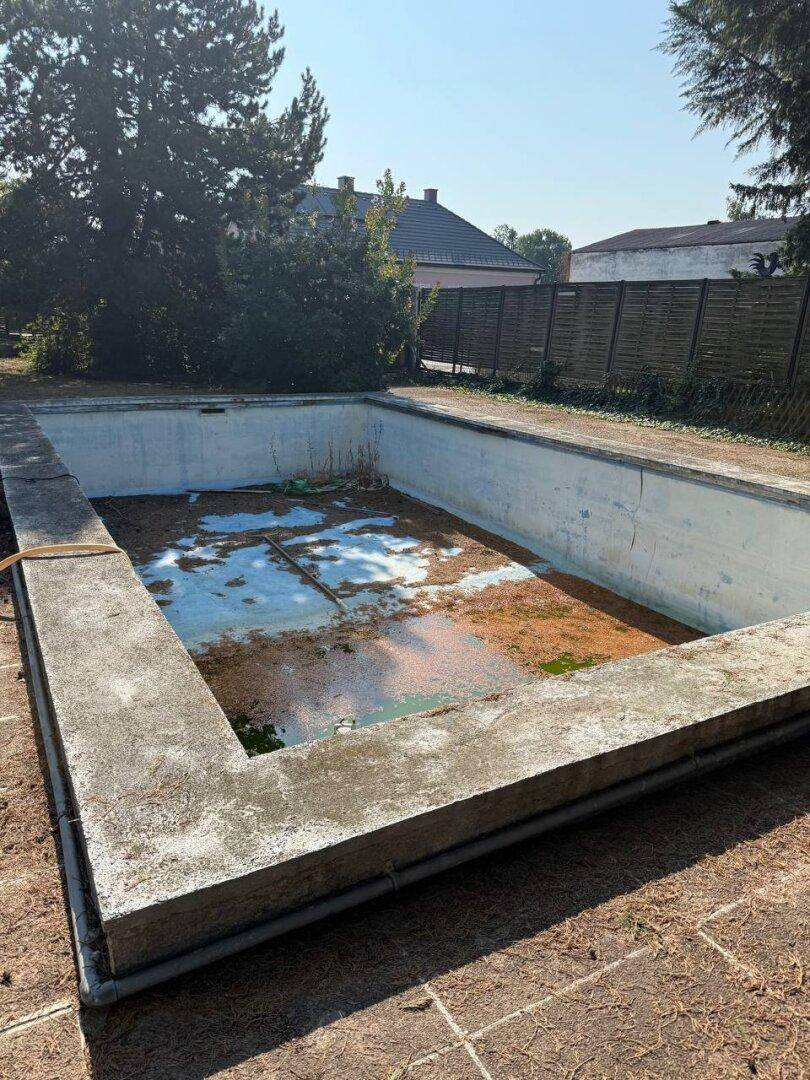 Nahaufnahme des leeren Schwimmbeckens im Garten, das Renovierung benötigt.