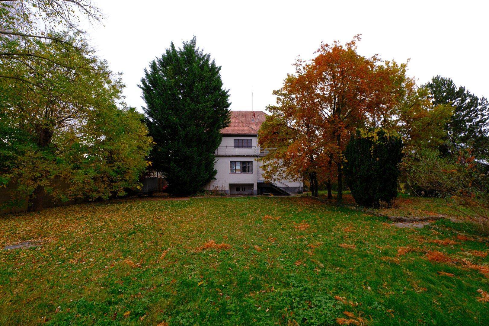 Blick vom Garten auf die Rückseite des Hauses mit einem kleinen Balkon und herbstlichen Bäumen.