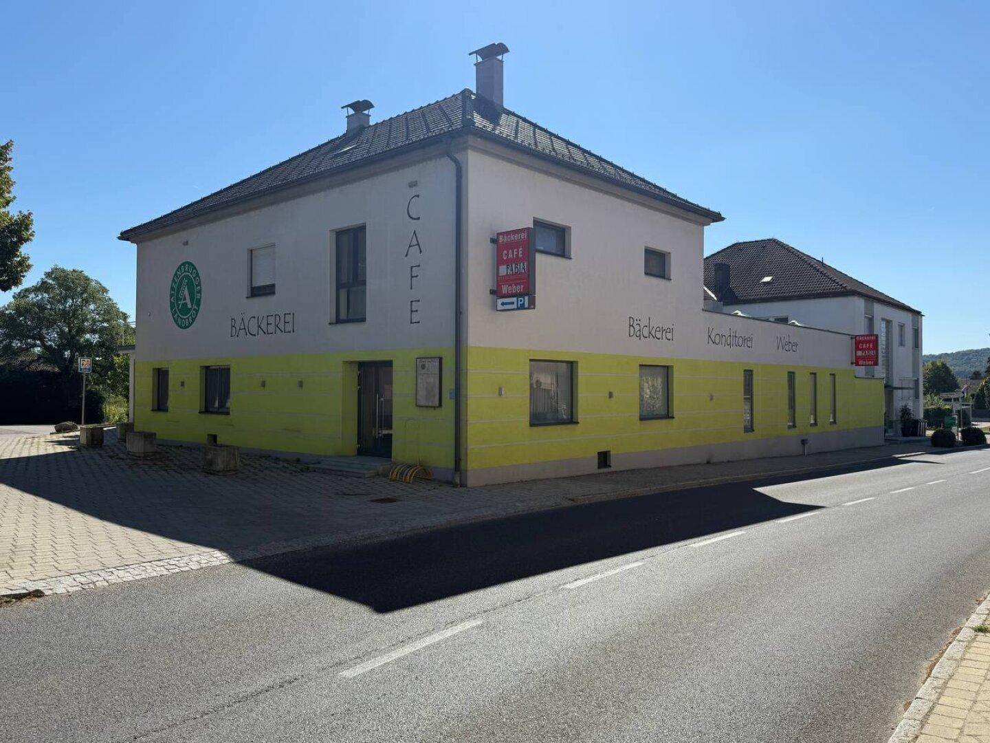 Gebäudeansicht von der Straße mit gelb-weißer Fassade und Beschilderung für Bäckerei und Café.