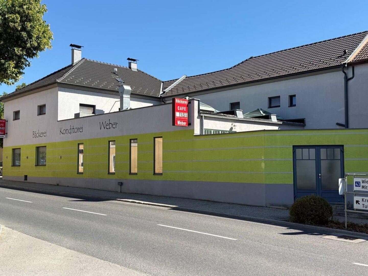 Seitenansicht des Gebäudes mit gelb-grüner Fassade und Beschilderung für Bäckerei und Konditorei.
