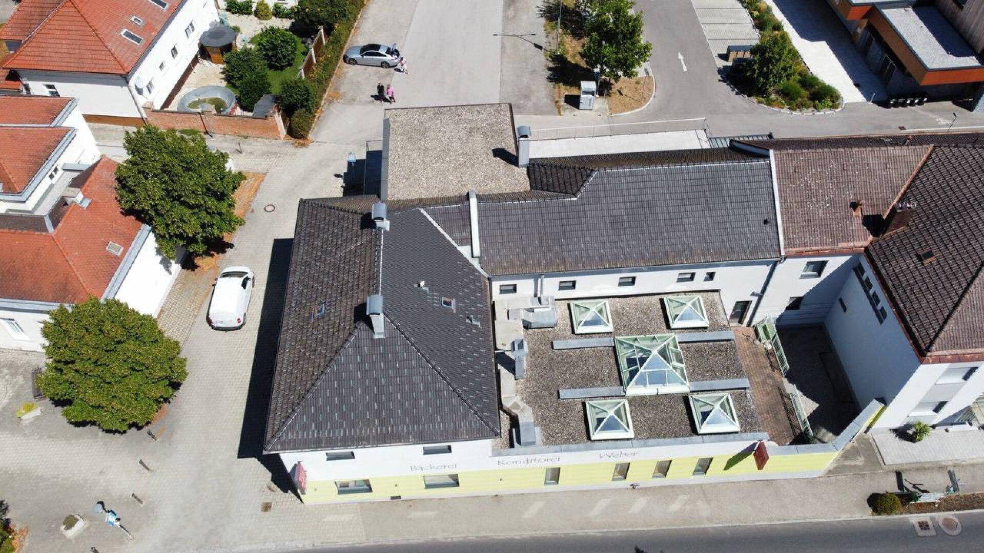 Luftaufnahme des Gebäudes mit Flachdach und mehreren Oberlichtern in einer städtischen Umgebung.