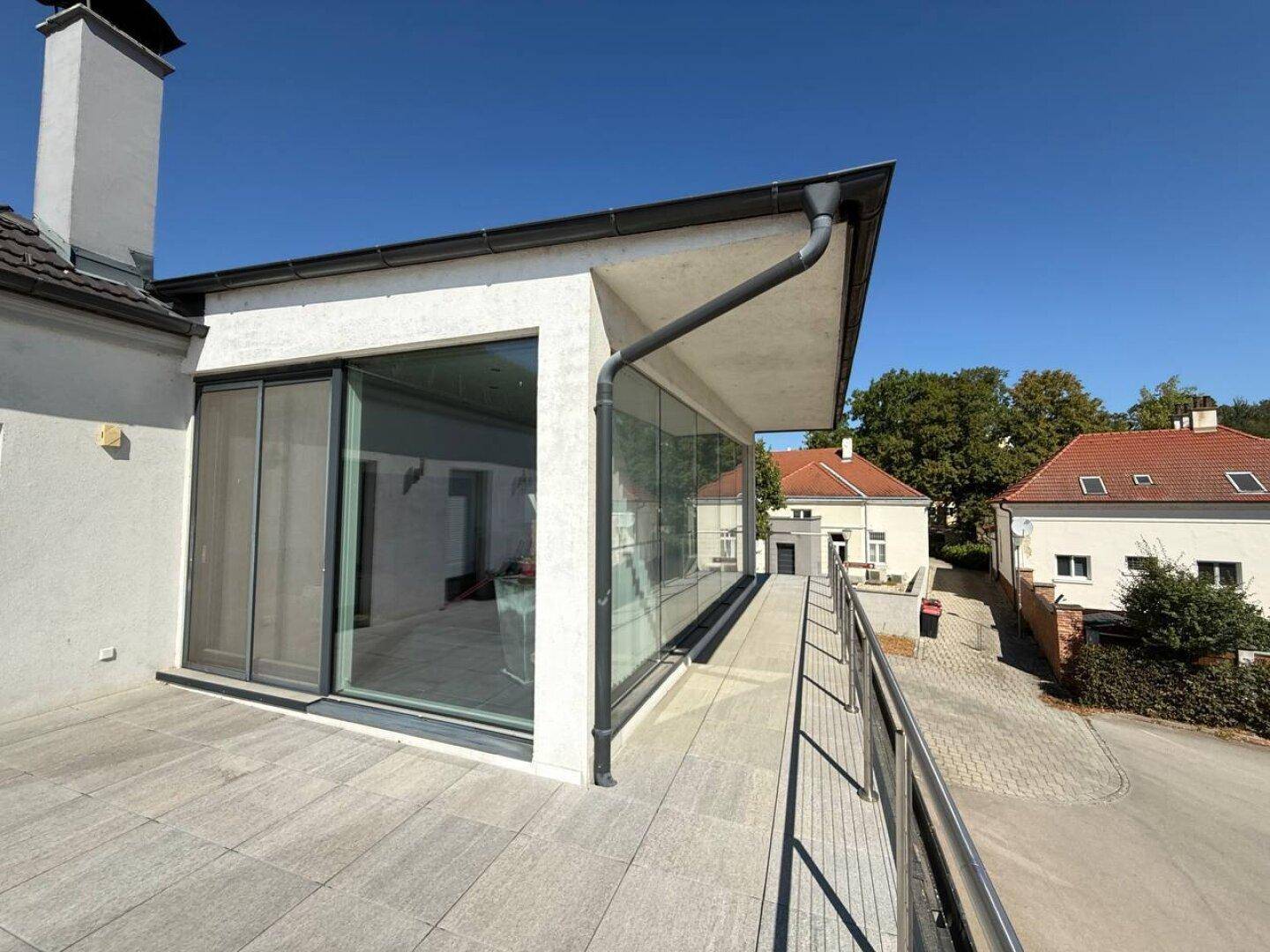 Blick von der Terrasse auf die moderne Glasfassade des Gebäudes und die darunterliegende Straße.