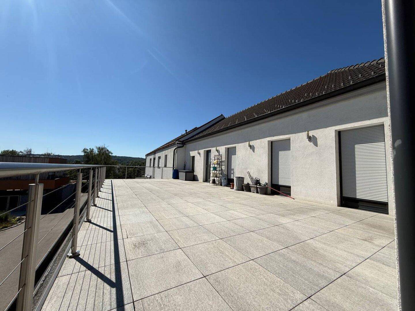 Weitläufige, geflieste Terrasse mit moderner Metallbrüstung und Blick auf die Umgebung.