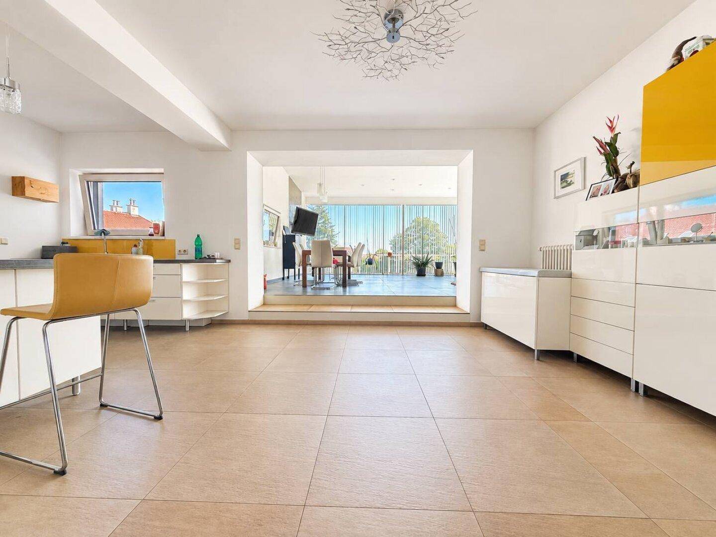 Helle Küche mit beigen Fliesen, weißen Schränken und offenem Blick in den Wohnbereich.