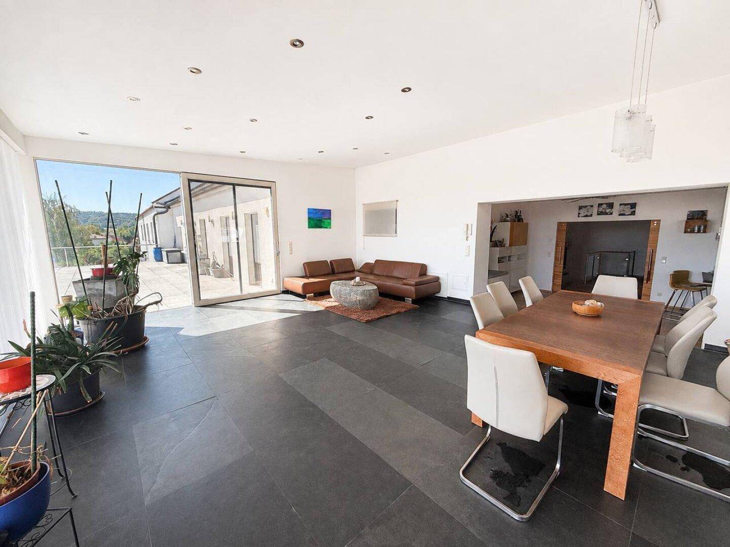Geräumiger Wohn- und Essbereich mit braunem Sofa, Esstisch und direktem Zugang zur sonnigen Terrasse.