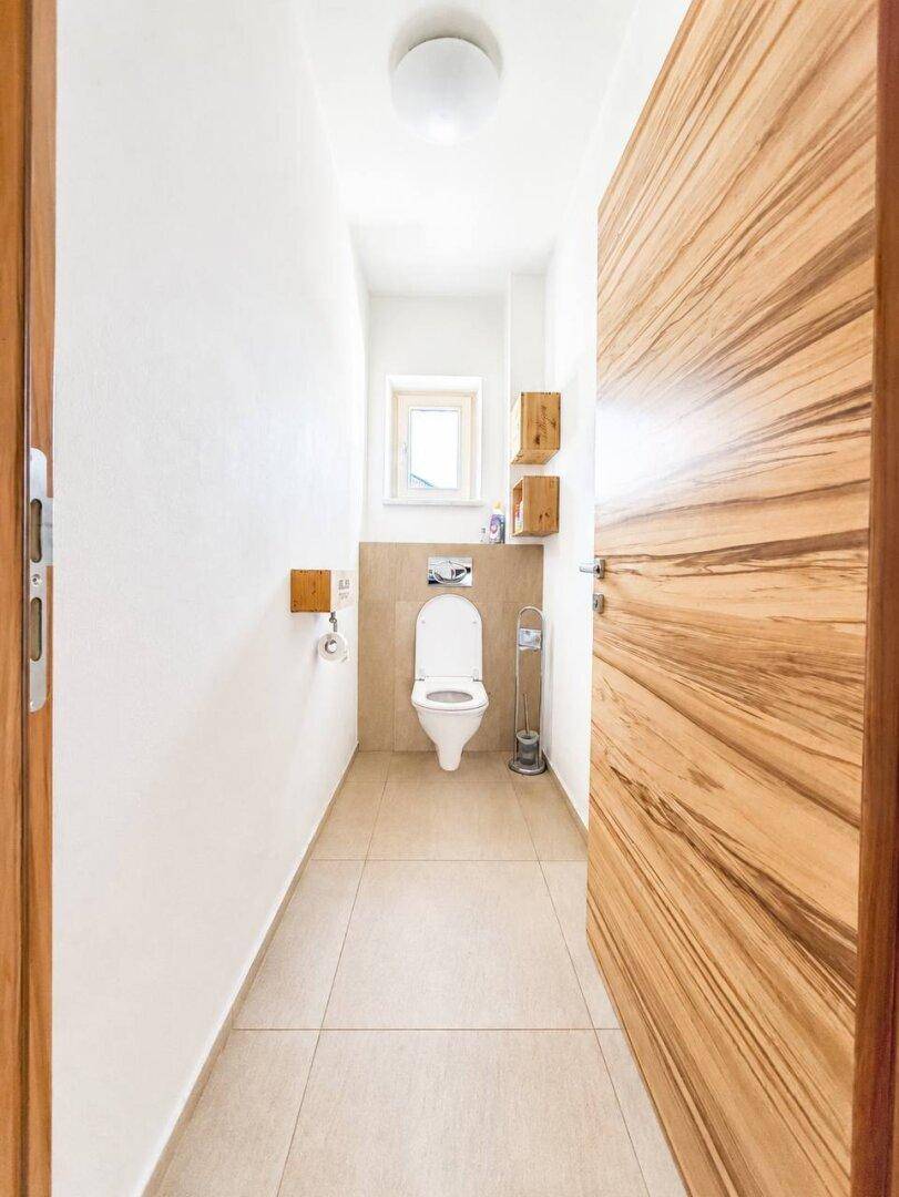 Kleines Gäste-WC mit wandhängender Toilette, beigen Fliesen und Fenster.