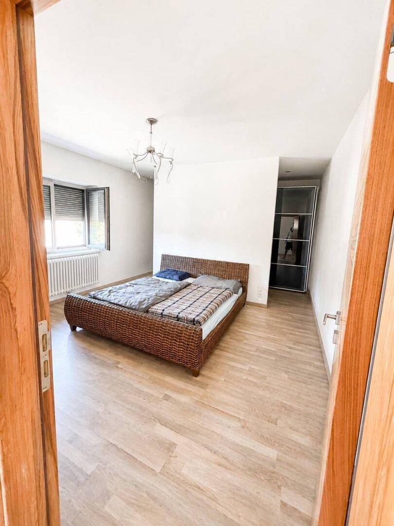 Schlafzimmer mit Rattanbett, Laminatboden und einem Erkerfenster.