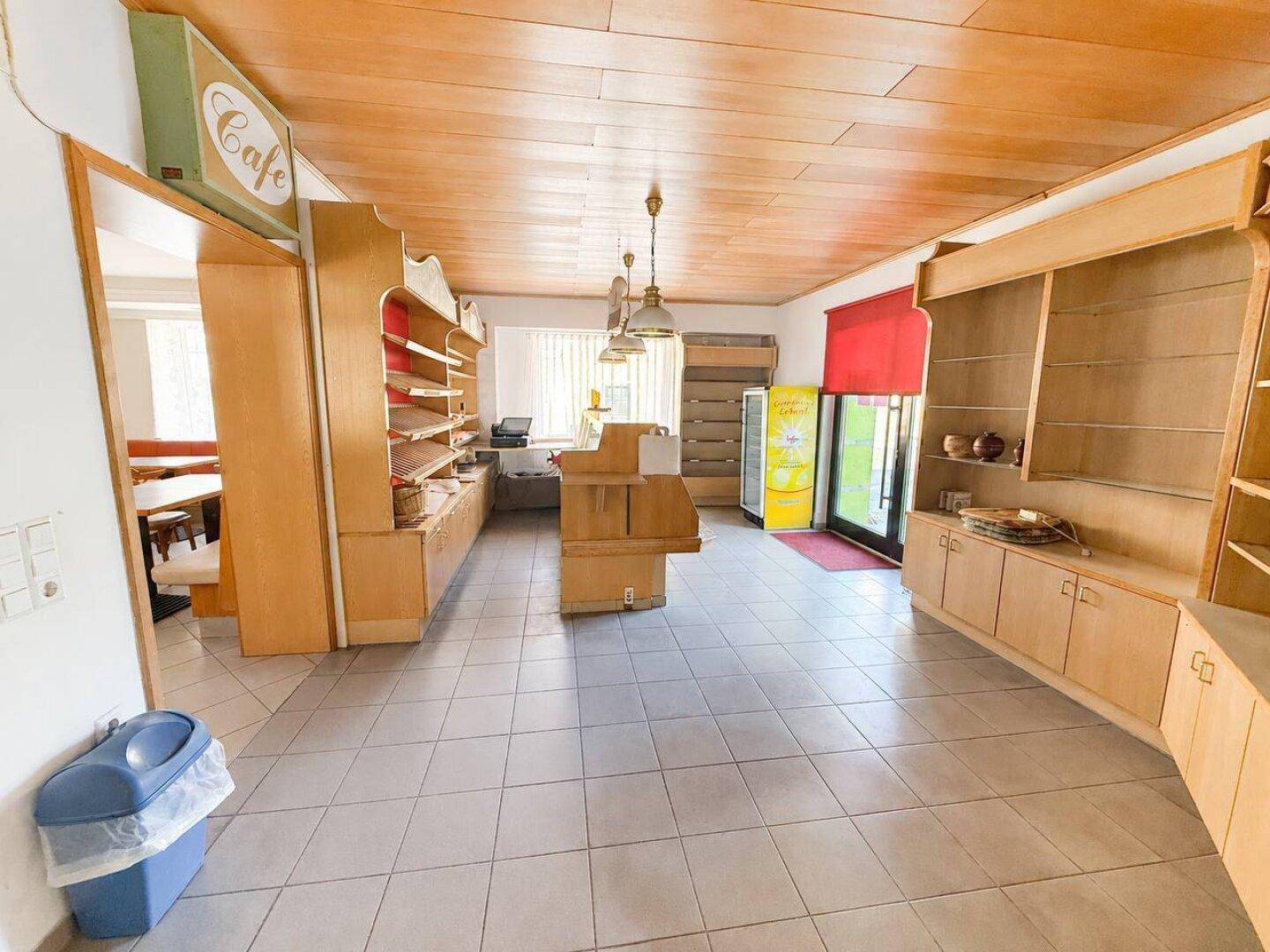 Geräumiger Ladenbereich mit Holzdecke, Fliesenboden und Verkaufstheke, ideal für ein Café oder eine Bäckerei.