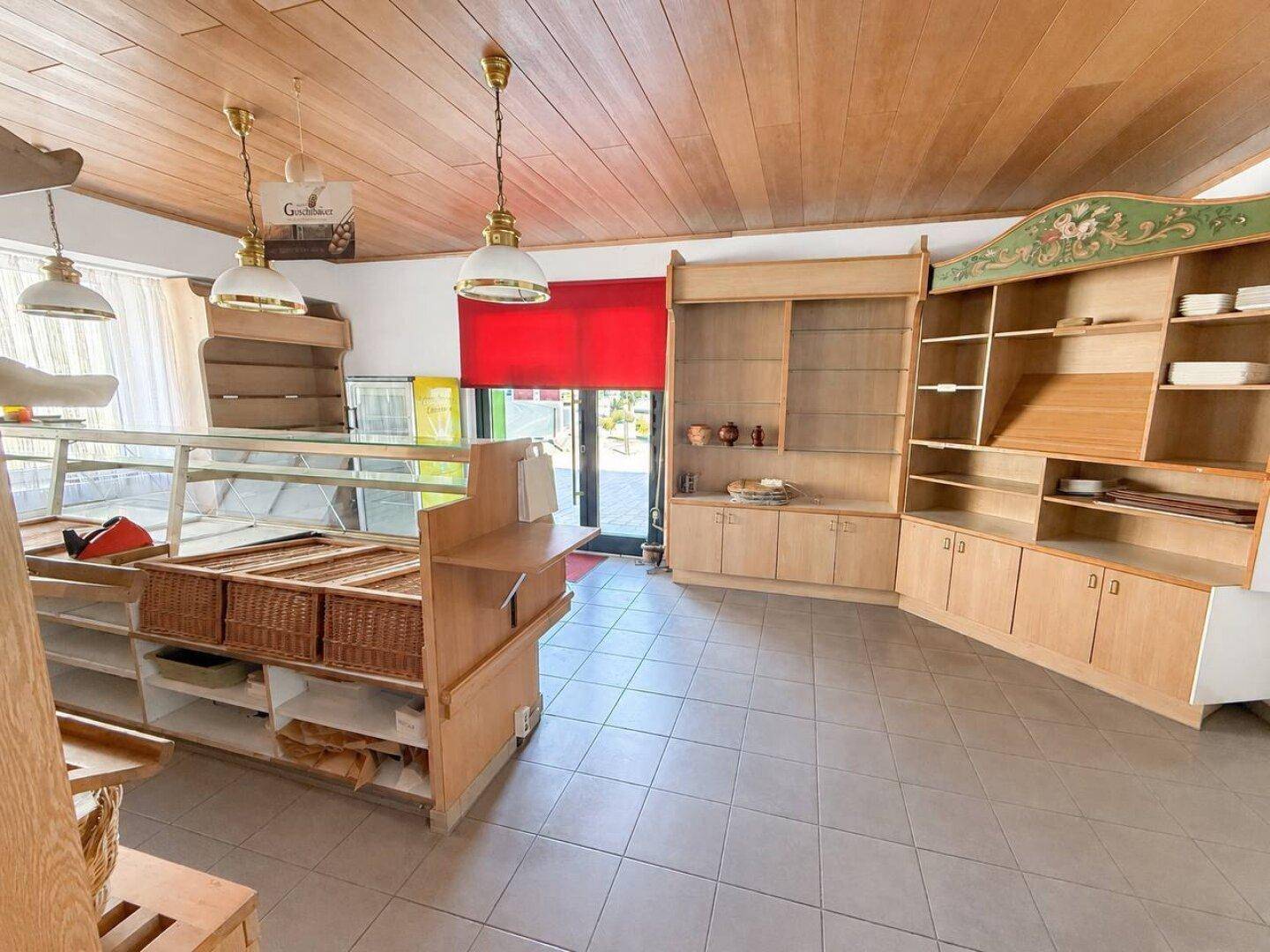 Ladenfläche mit Holzdecken, Fliesenboden und leeren Regalen, bereit für neue Nutzung.