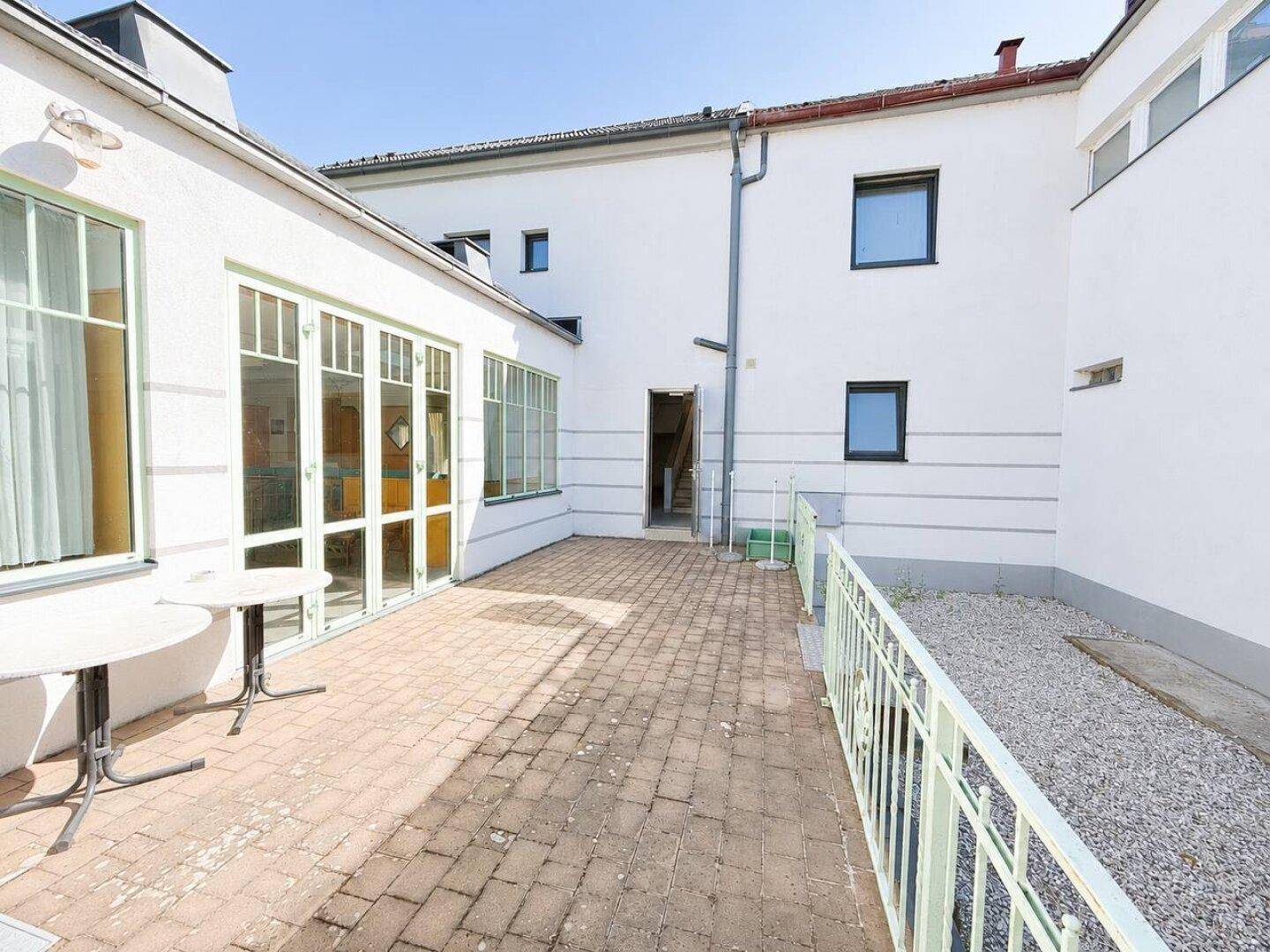 Gepflasterte Terrasse mit Sitzgelegenheiten im Freien und Blick auf das Gebäude.