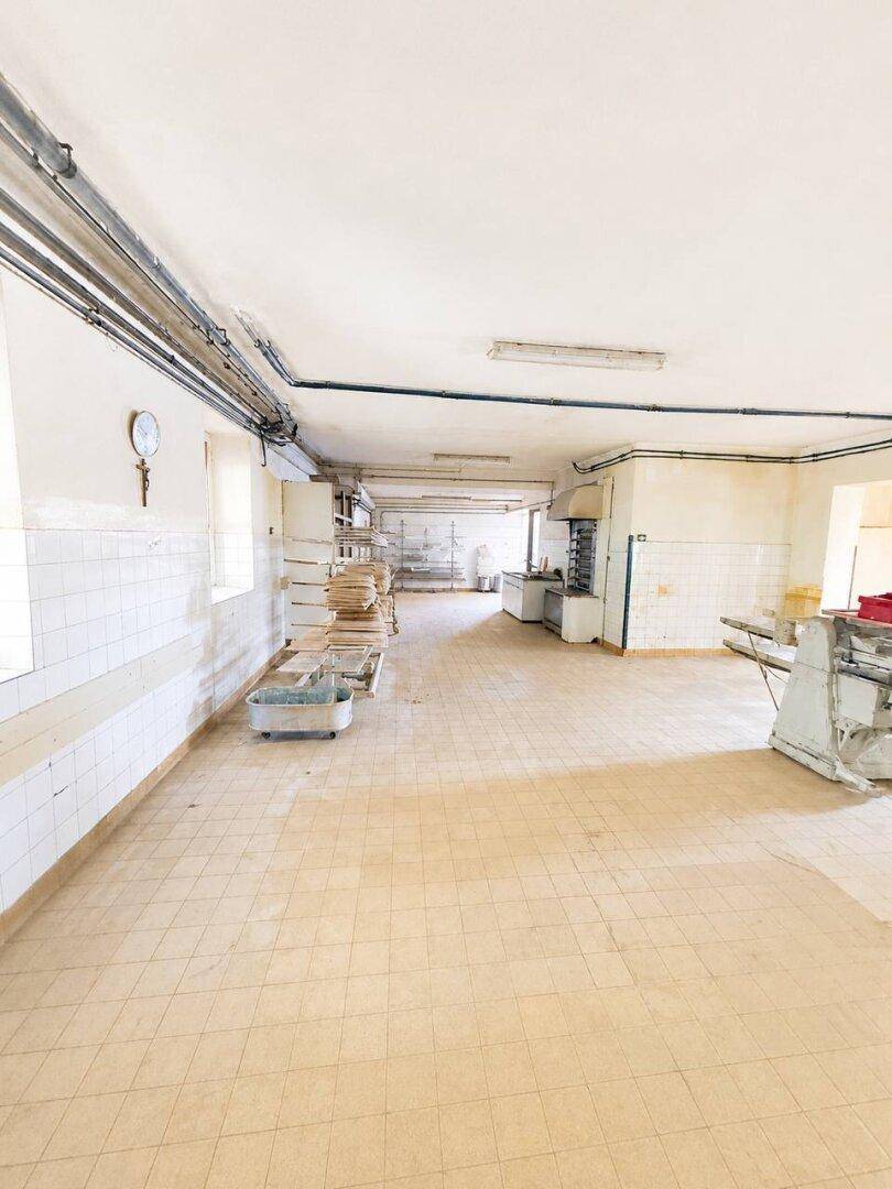 Langer Wirtschaftsraum mit Fliesenwänden, Regalen und industriellen Arbeitsflächen.