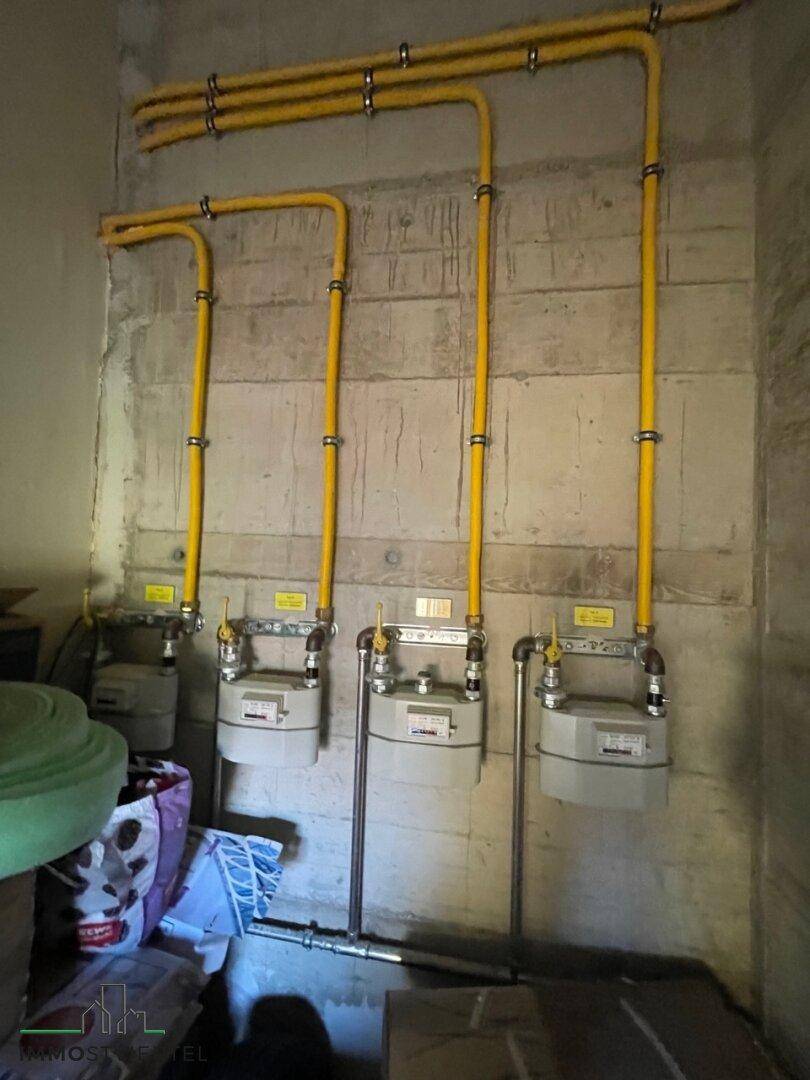 Technikraum mit mehreren Gaszählern und sichtbaren gelben Gasleitungen an der Wand.