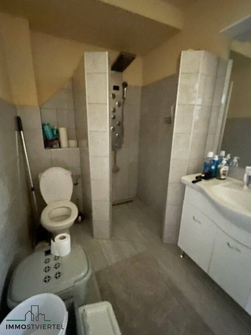 Badezimmer mit Toilette, Einzelwaschbecken und Duschbereich, unter einer Dachschräge.
