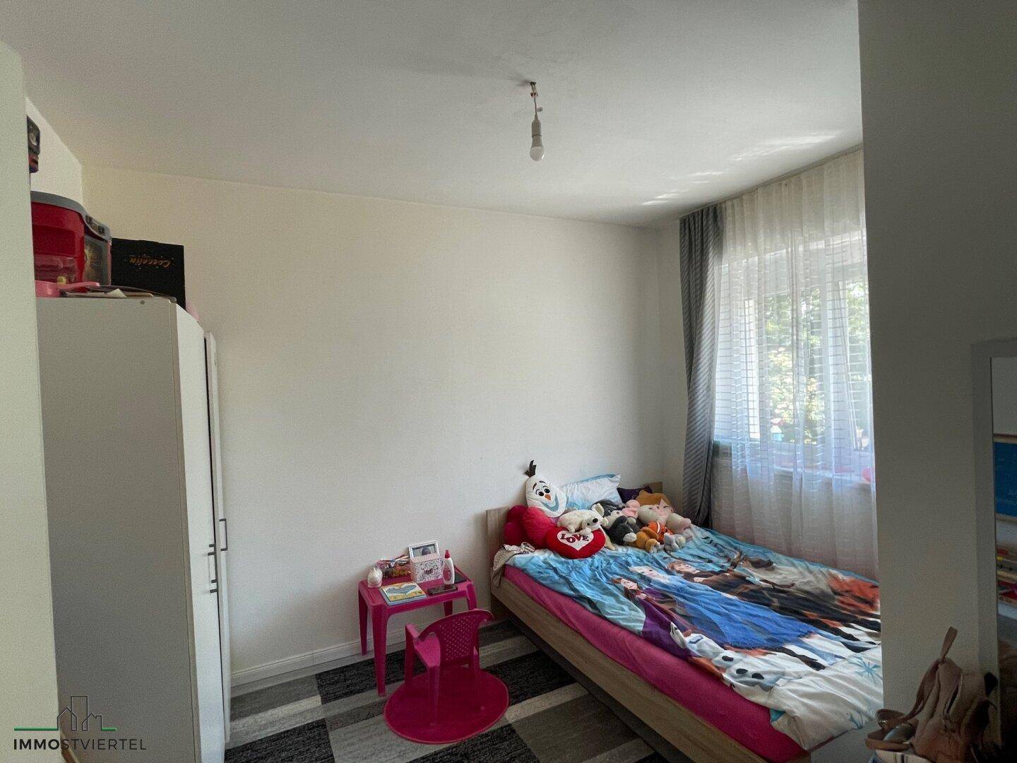 Kinderzimmer mit Einzelbett, weißem Kleiderschrank und Fenster, hell und freundlich.