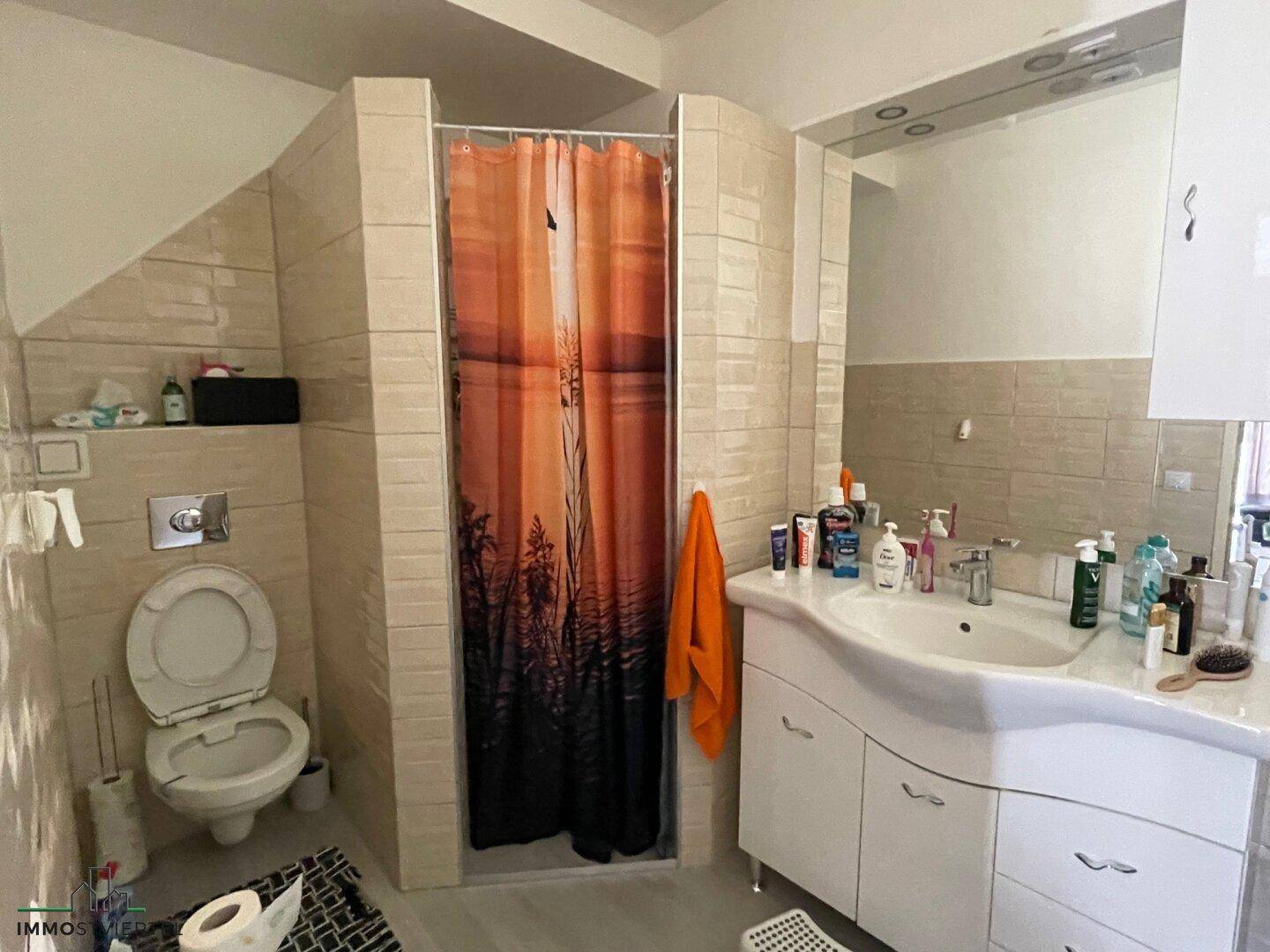 Badezimmer mit Toilette, Einzelwaschbecken und Duschbereich mit Vorhang.
