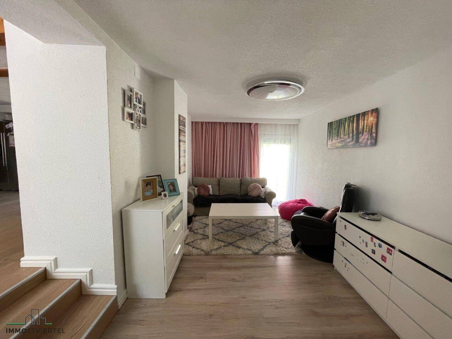 Gemütliches Wohnzimmer mit Sofa, Couchtisch und großem Fenster mit rosa Vorhängen.