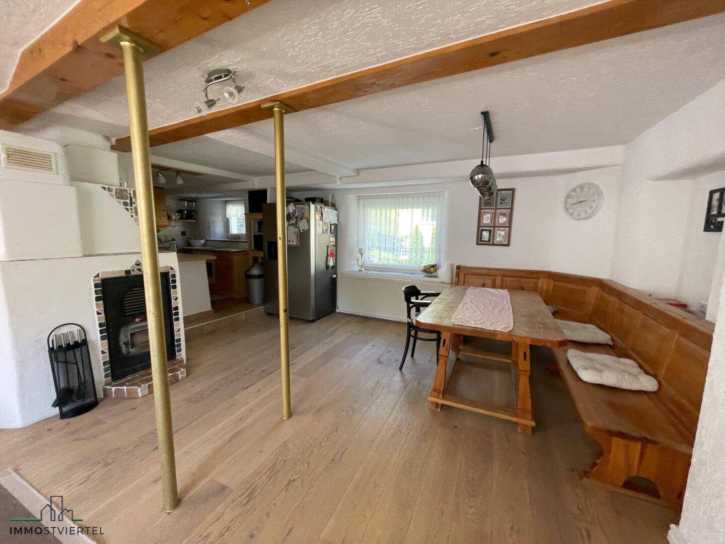 Rustikaler Essbereich mit Eckbank, Holztisch und traditionellem Kachelofen unter Holzbalken.