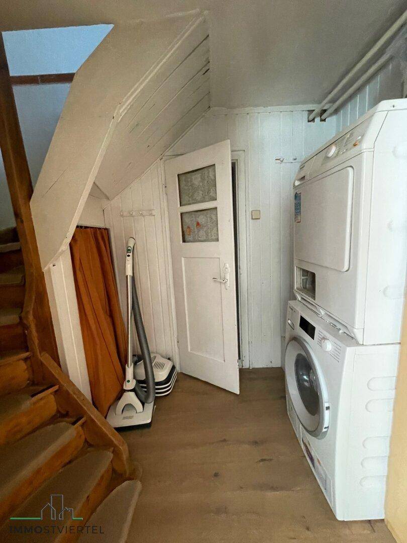Waschküche unter der Treppe mit Waschmaschine und Trockner, umgeben von Holzverkleidung.