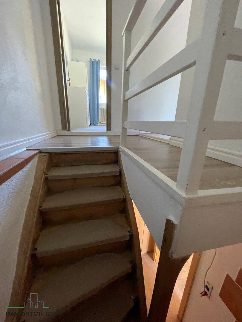 Holztreppe führt zu einem oberen Flur mit hellem Holzboden und weißem Geländer.