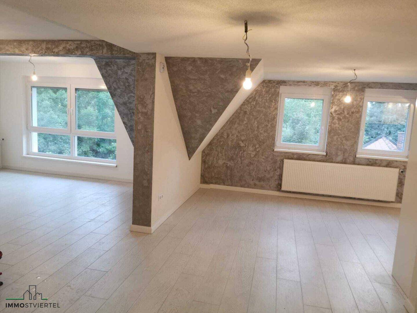 Heller, leerer Raum mit Holzboden, weißen Wänden und strukturierten grauen Akzenten.