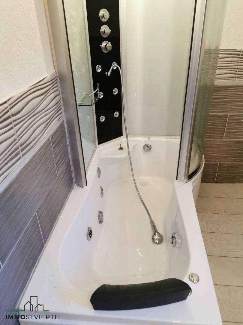 Eckbadewanne mit Duschabtrennung, möglicherweise eine Whirlpool-Funktion.