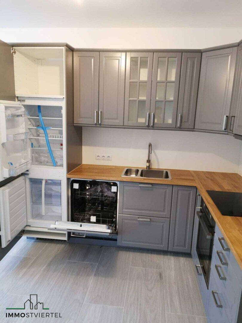 Graue Küche mit Holzarbeitsplatten, integriertem Kühlschrank und Geschirrspüler.