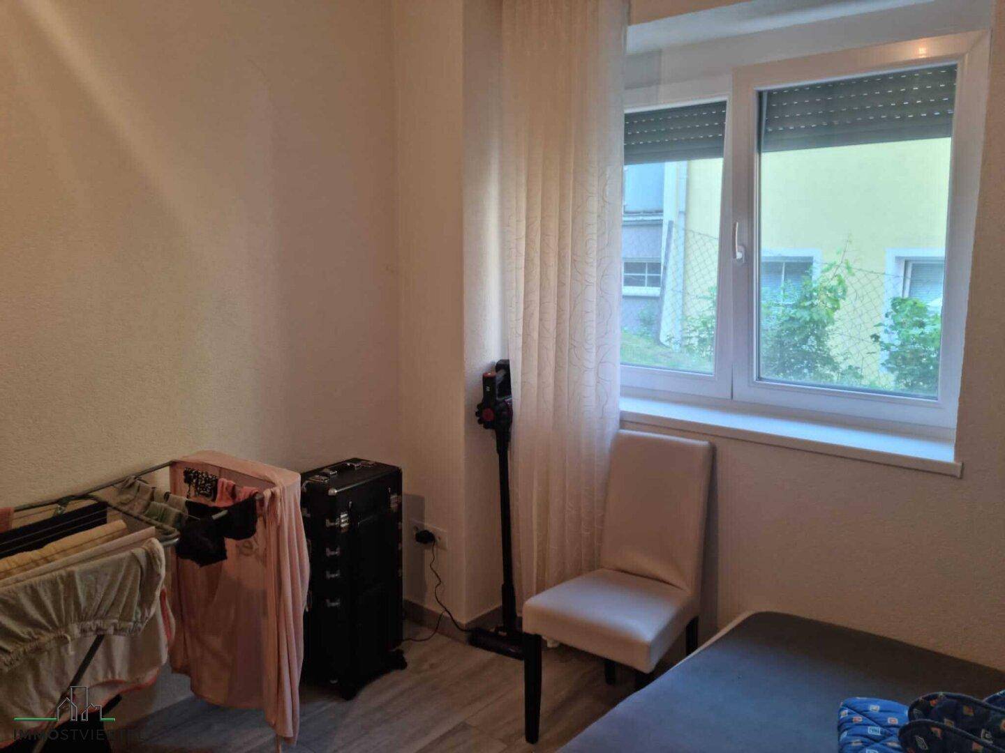 Kleines Zimmer mit Fenster, Stuhl und Wäscheständer, möglicherweise als Abstellraum genutzt.