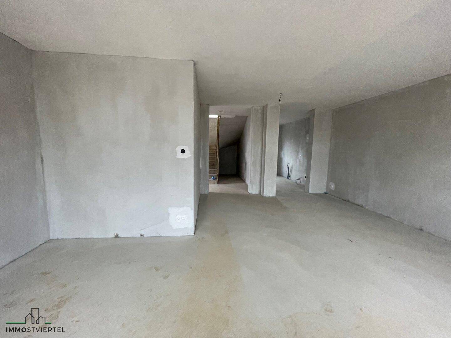 Langer, unfertiger Flur mit Blick auf die Treppe im Hintergrund.