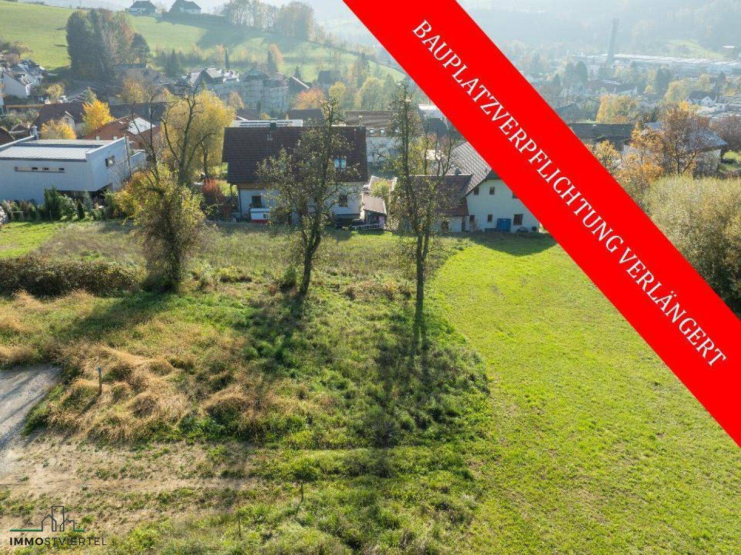 Grünes Baugrundstück mit Bäumen und Blick auf die umliegende Bebauung und Hügellandschaft.