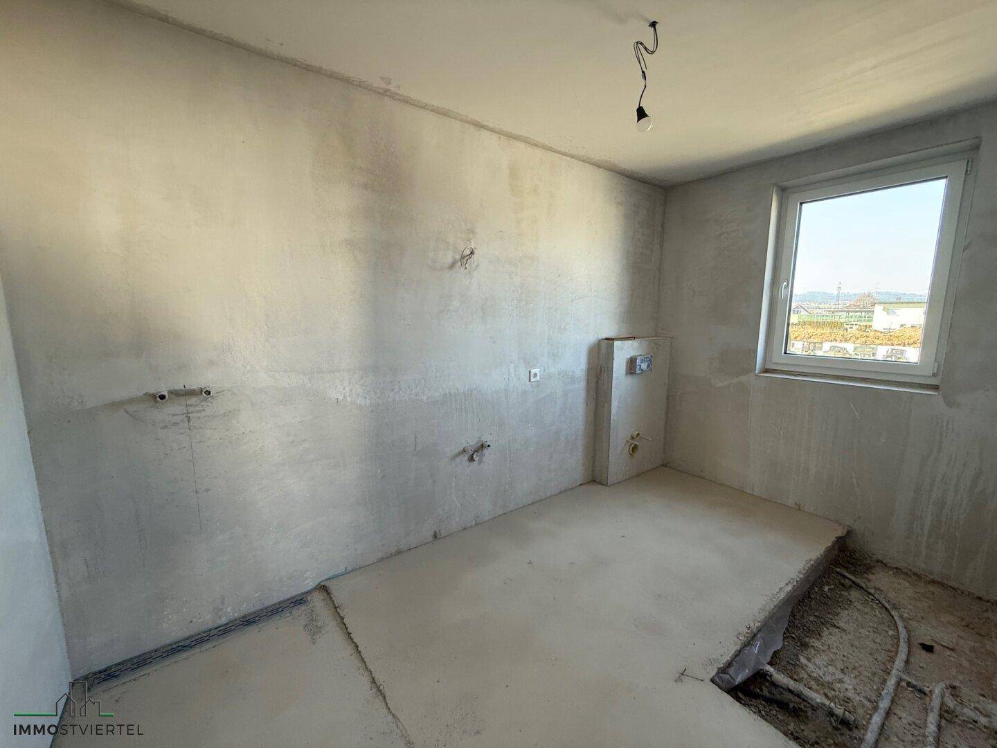 Unfertiges Badezimmer mit Rohinstallationen für Sanitäranlagen und einem Fenster.