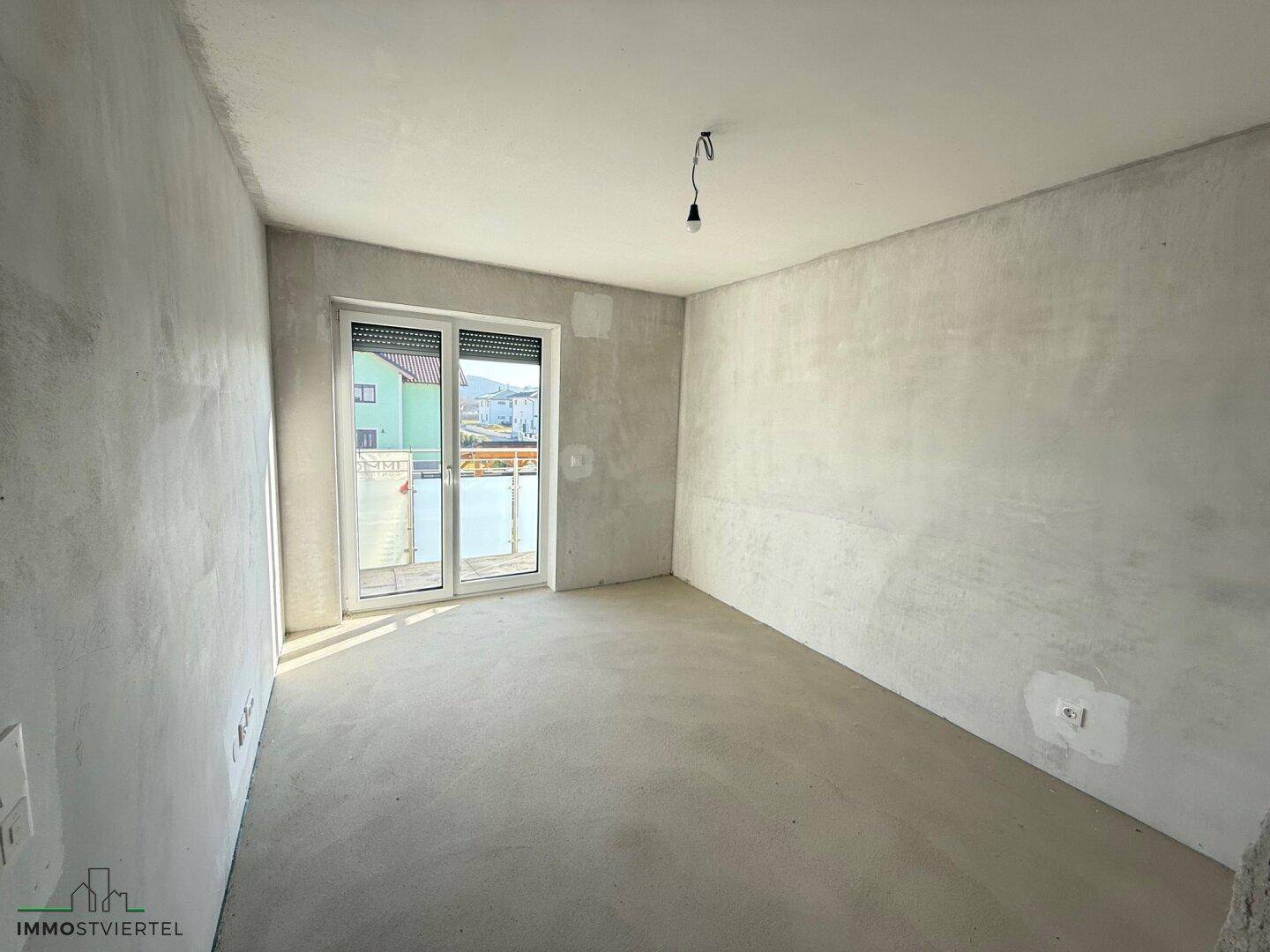 Unfertiger Raum mit Zugang zu einem französischen Balkon, der Tageslicht spendet.