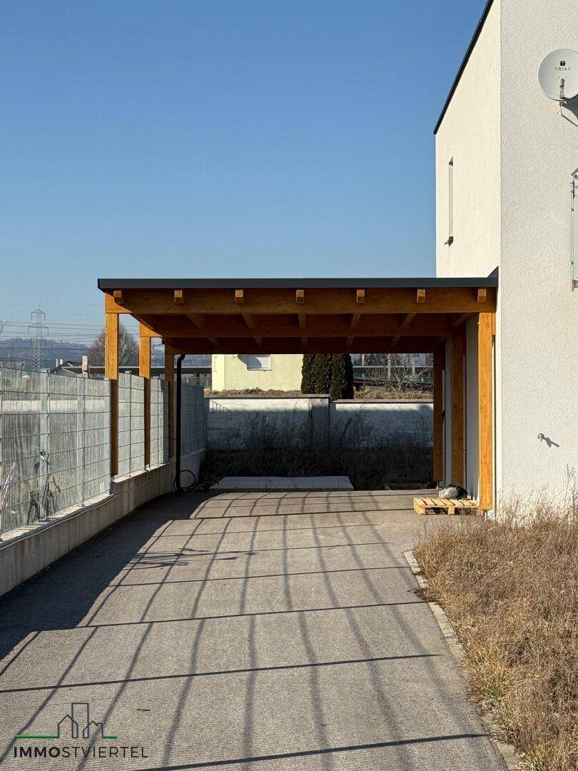 Neu errichteter Holzcarport neben einem modernen Einfamilienhaus mit Zufahrt.