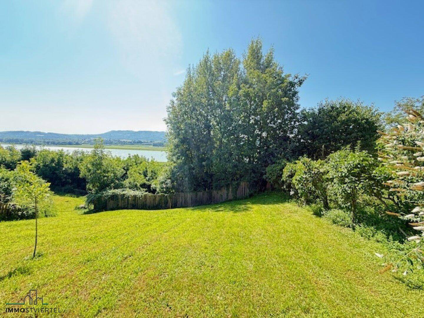 Großer Gartenbereich mit Rasenfläche und Blick auf den See und die umliegende Landschaft.