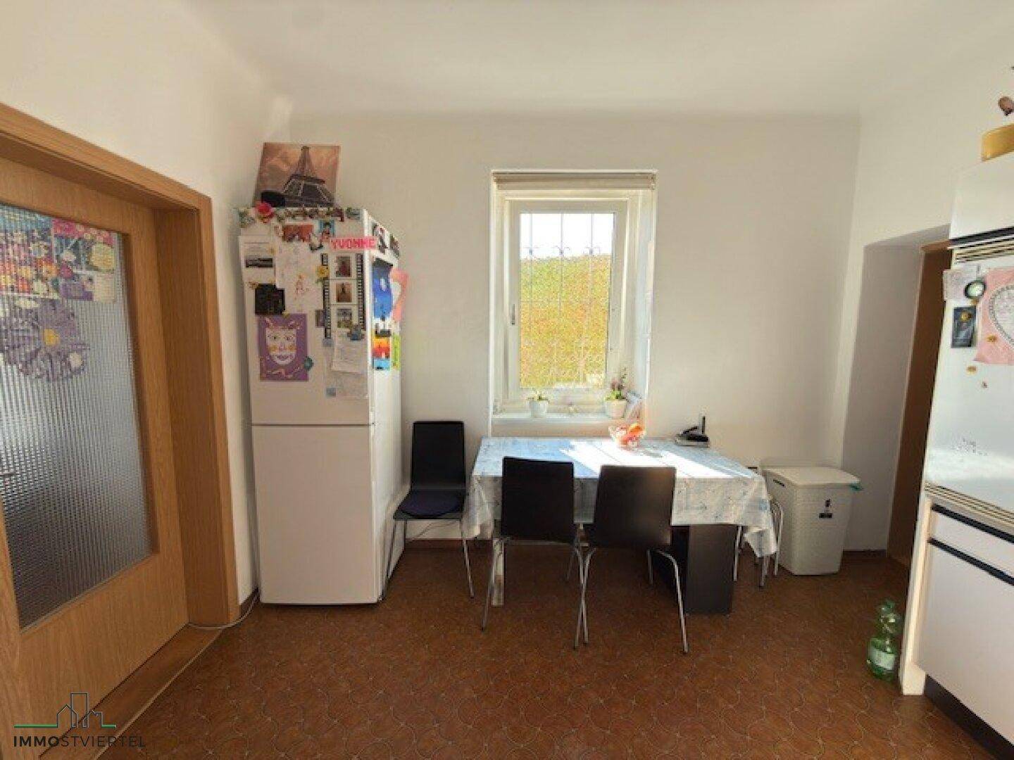 Küche mit Esstisch, Kühlschrank und Fenster, das Tageslicht spendet.