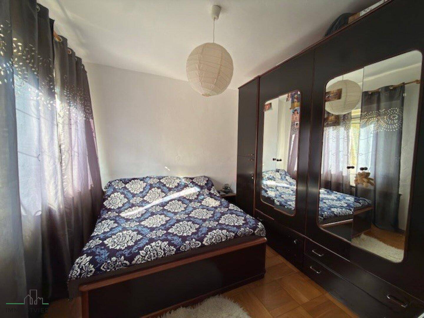 Schlafzimmer mit Doppelbett, großem Spiegelschrank und Vorhängen.