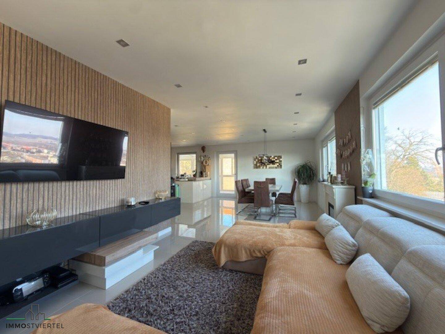 Geräumiger Wohnbereich mit Holzwand, großem Sofa und offener Verbindung zur Küche.
