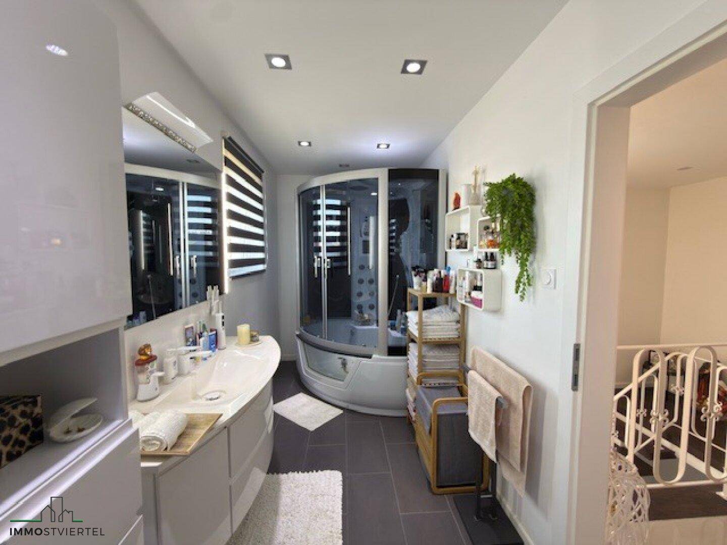 Modernes Badezimmer mit Doppelwaschbecken, großer Duschkabine und dunklen Fliesen.