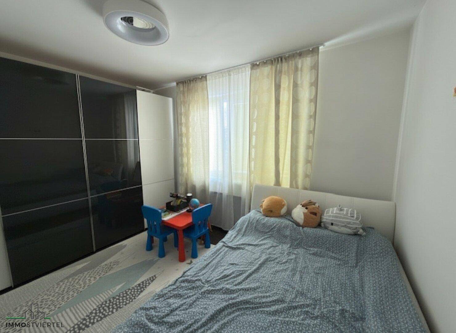 Kinderzimmer mit Bett, Schrank und Fenster, das viel Tageslicht hereinlässt.