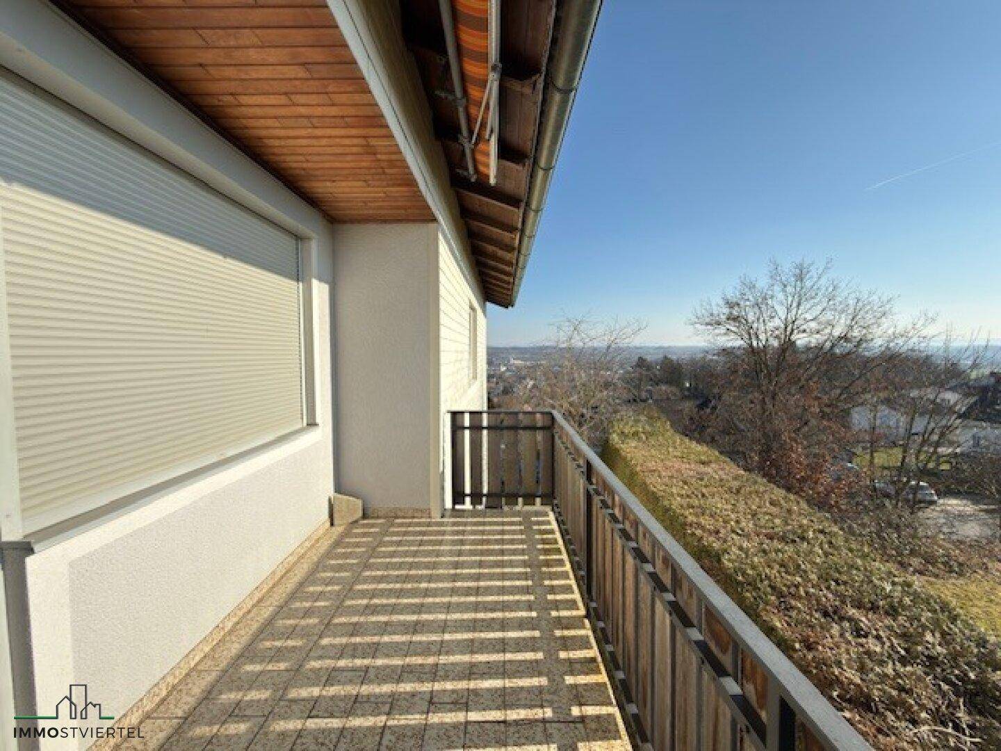 Geräumiger Balkon mit Fliesenboden, Holzgeländer und weitem Blick über die Landschaft.