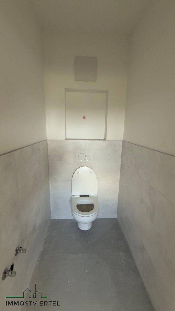 Modernes Gäste-WC mit Wand-WC und hellen Fliesen, noch ohne Waschbecken.