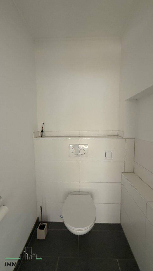 Sauberes WC mit wandhängender Toilette und modernen Fliesen an Wand und Boden.