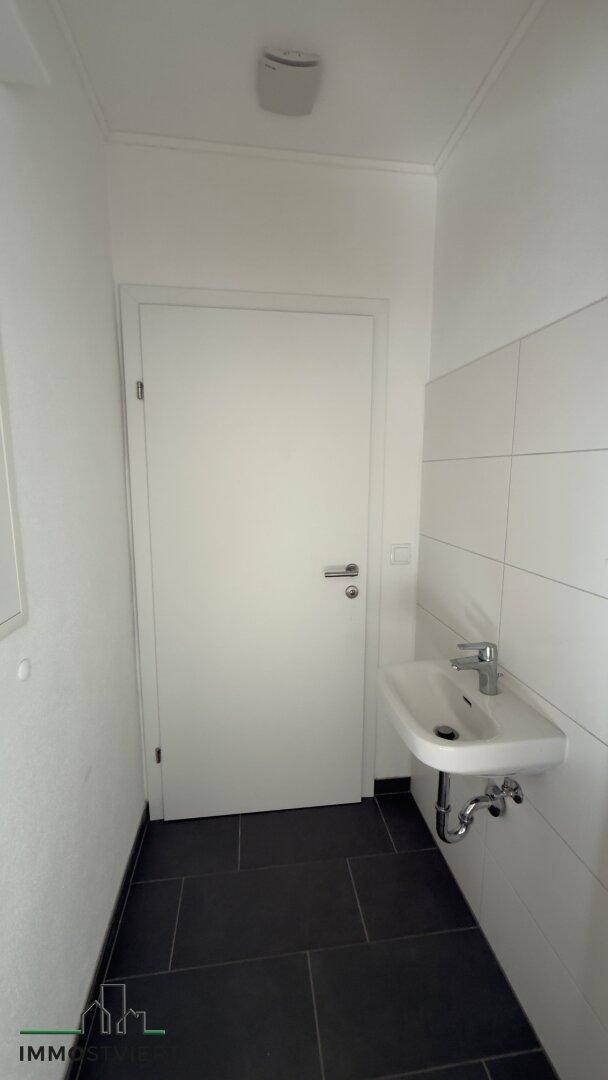 Modernes Gäste-WC mit weiß gefliesten Wänden und dunklem Boden.