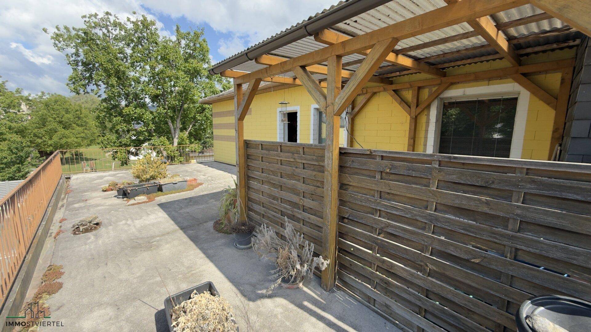 Große, gepflasterte Terrasse mit Holzpergola und Blick ins Grüne, ideal für Entspannung im Freien.