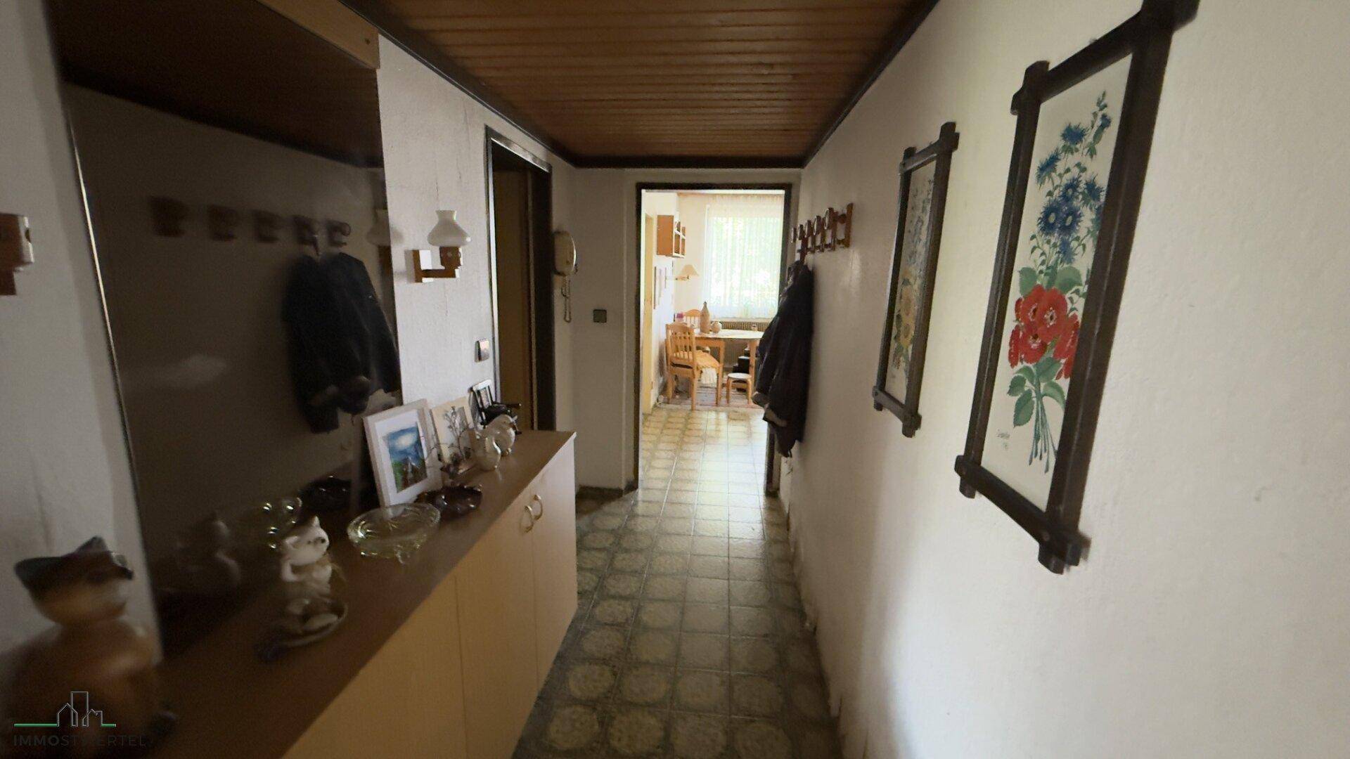 Flur mit Holzdecke, gefliestem Boden und Garderobe, der zu weiteren Räumen führt.