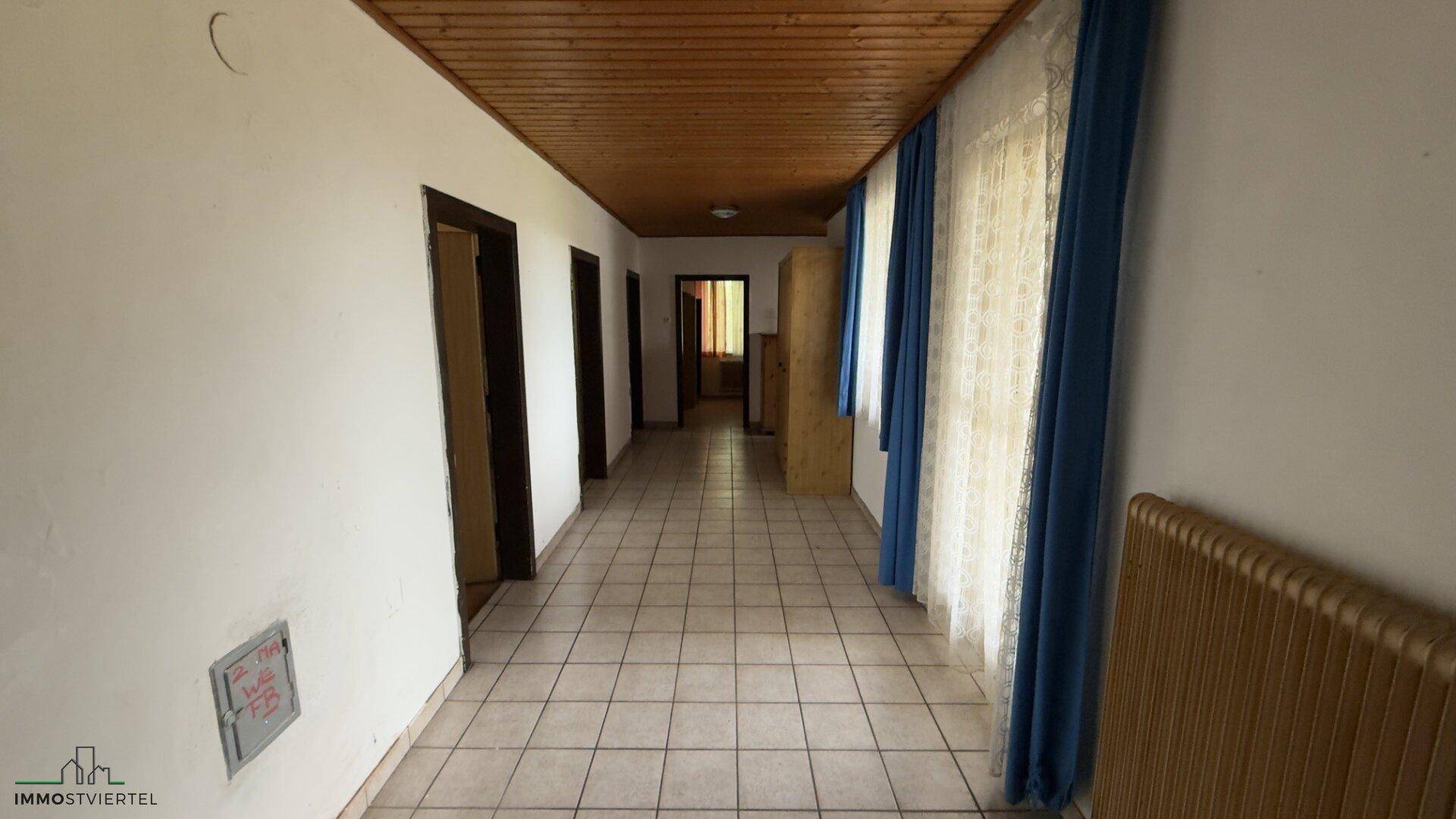 Langer Flur mit gefliestem Boden, Holzdecke und Fenstern, der viel natürliches Licht bietet.